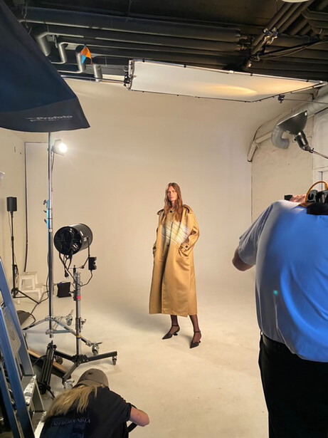 Professional studio portrait setup with model wearing gold dress and photographer adjusting lighting equipment.