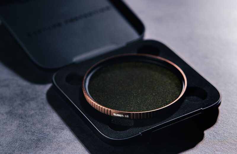 Rose gold bangle bracelet with textured surface displayed in open black presentation box on gray surface.