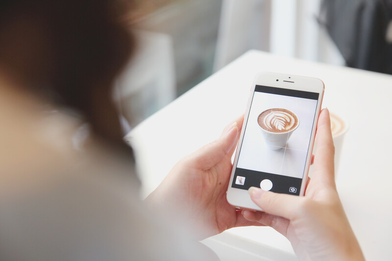 Person holding smartphone displaying a close-up photo of latte art on a coffee cup.