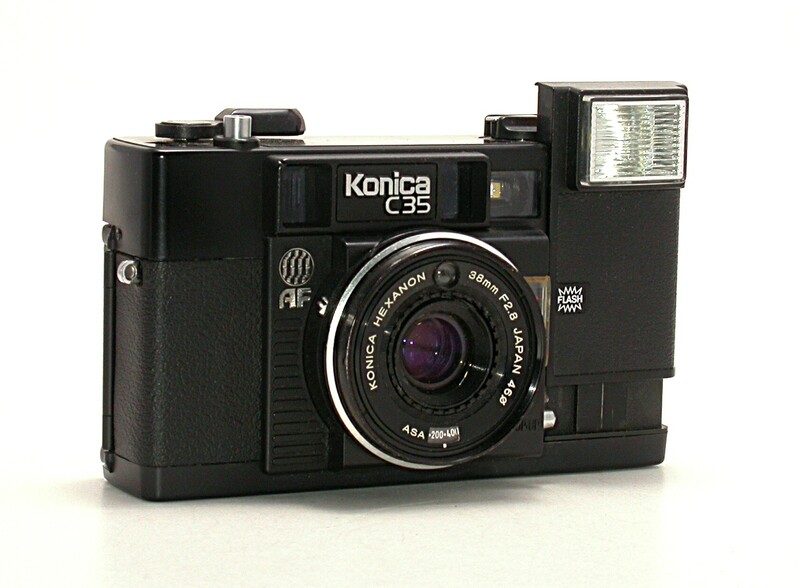 Konica C35 rangefinder camera with flash and lens attachment on white background.