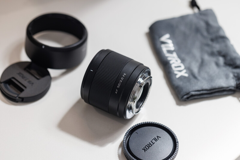 Telephoto lens with lens cap, hood, and cleaning cloth displayed on white surface.