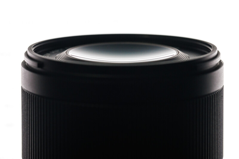Close-up of a black cylindrical lens barrel with ridged focusing ring and glass front element.