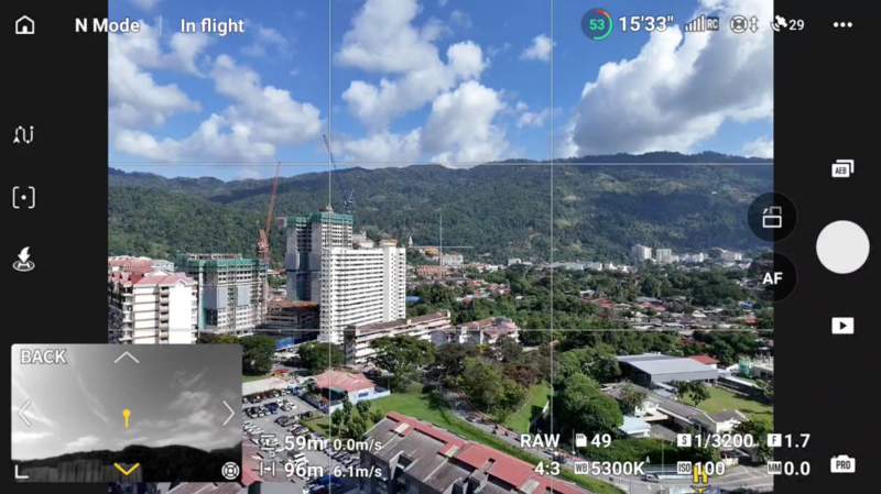 Screenshot of smartphone camera app in raw mode showing urban cityscape with mountains and buildings in bright daylight.