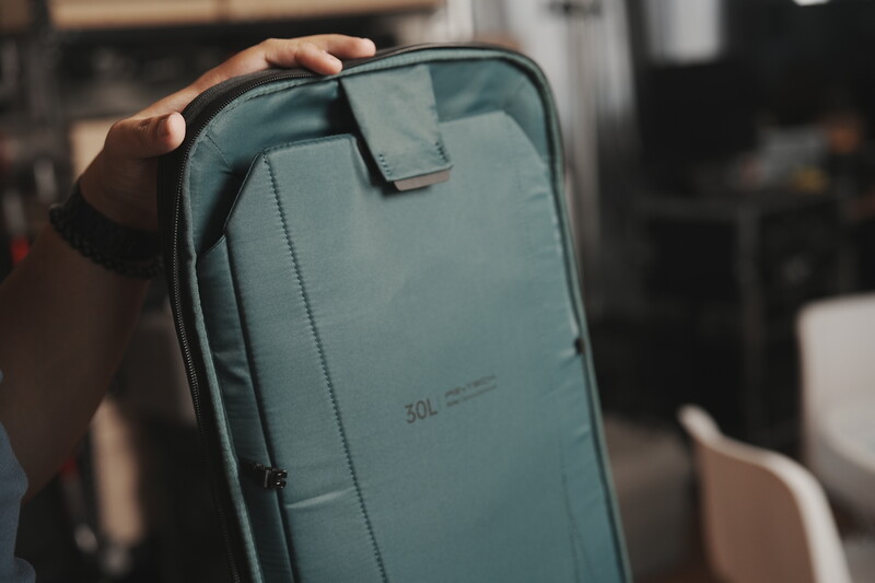 Person holding a light blue camera bag or backpack with zippered pockets and a carrying handle.