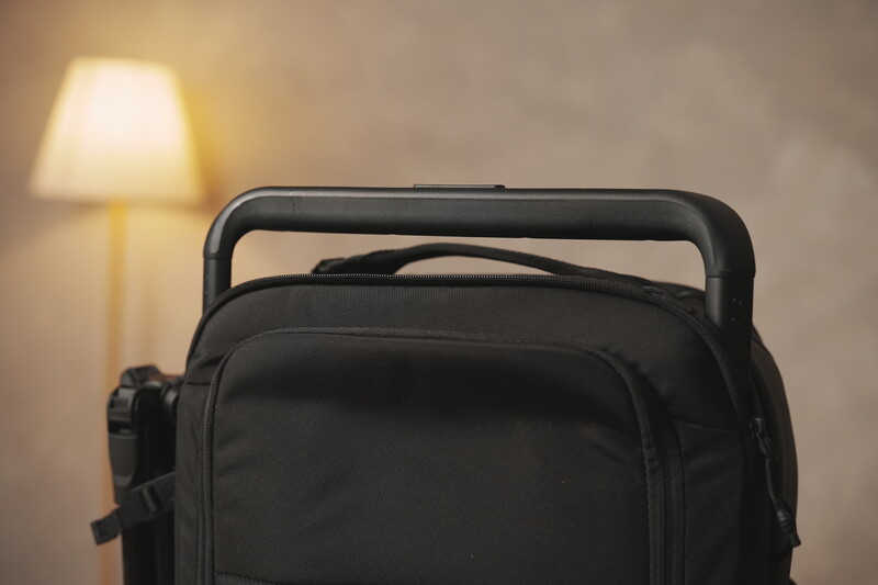 Black camera backpack with carry handle displayed indoors against warm lamp lighting.