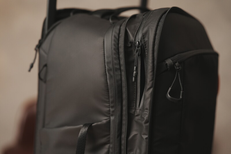 Dark gray camera backpack with multiple zippered compartments and side carabiners, photographed against a neutral background.