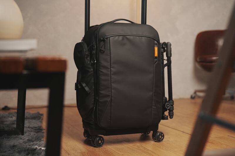 Black carry-on luggage with wheels and retractable handle positioned on wooden flooring indoors.