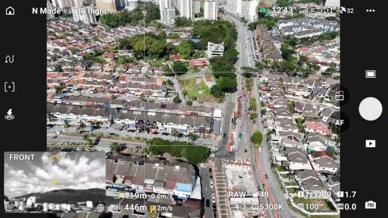 Aerial drone footage of dense urban neighborhood with residential buildings and a wide main street. Drone telemetry overlay visible.
