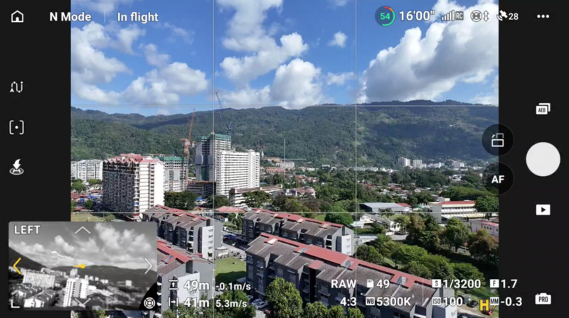 Screenshot of drone camera interface showing aerial view of mountainous urban valley with apartment buildings and green hillsides.