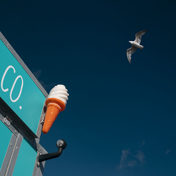 Turquoise buoy with orange and white top floating on deep blue ocean water, with a seabird flying above.