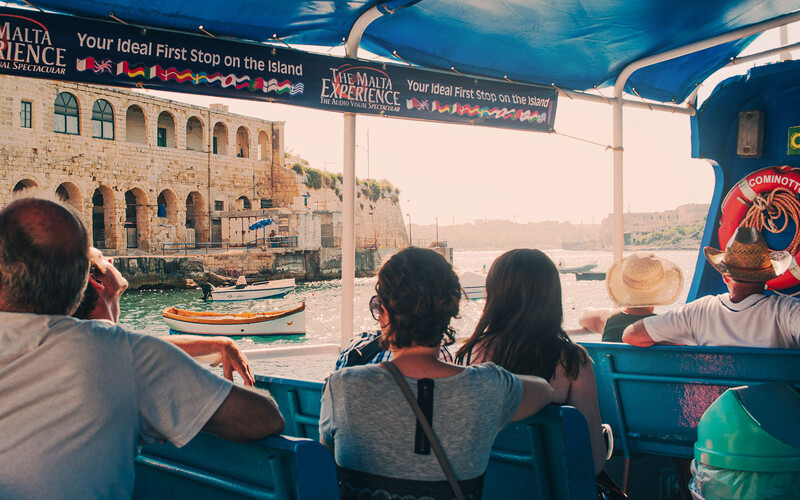 Passengers aboard a blue tour boat viewing historic waterfront architecture and moored fishing boats.