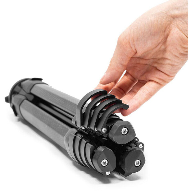 Hand holding a tripod head with multiple quick-release plates stacked together.