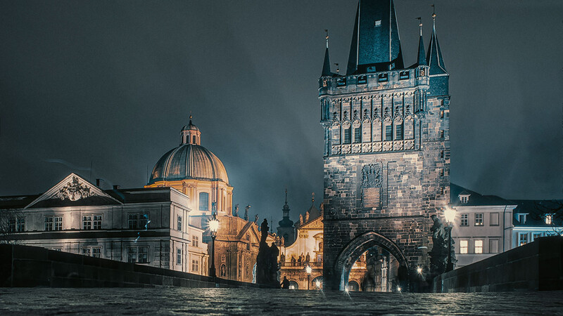 Gothic tower and classical dome reflected in dark water at dusk with dramatic stormy sky.