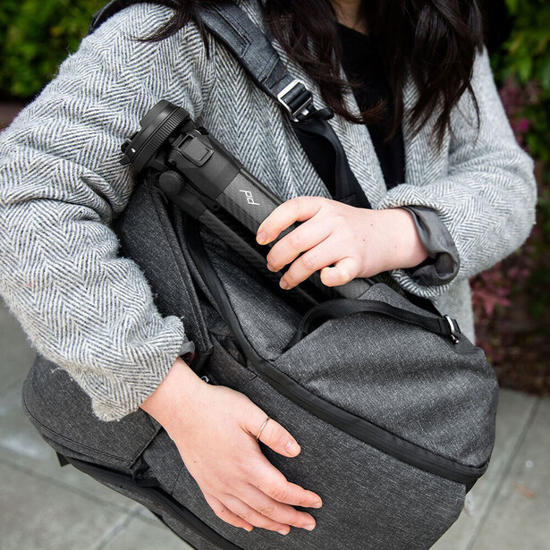 Person holding a dark camera bag with adjustable shoulder straps across their chest.