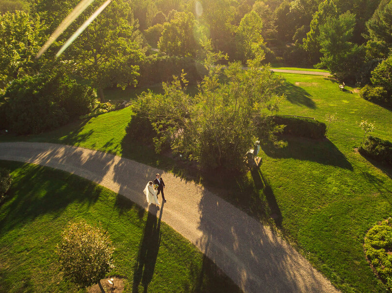 Aerial view of a couple walking on a narrow path through green meadows and forested areas.