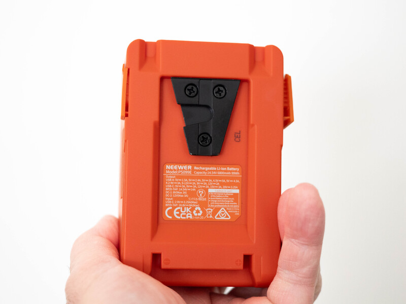 Hand holding a bright orange rectangular battery pack with black connector plate on back.