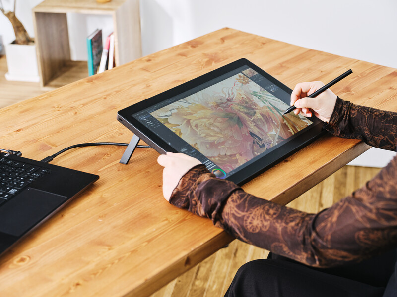 Digital artist using a stylus on a graphics tablet displaying a colorful portrait illustration.
