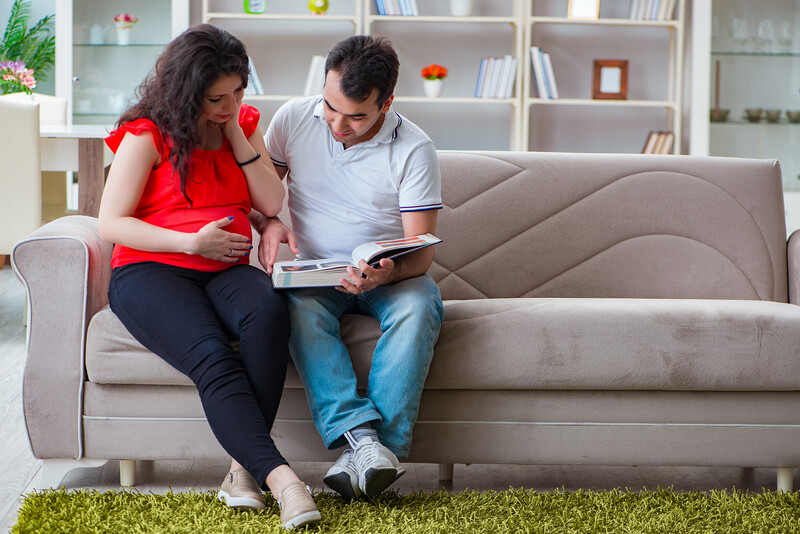 Couple sitting on a gray couch reviewing documents together in a bright living room.