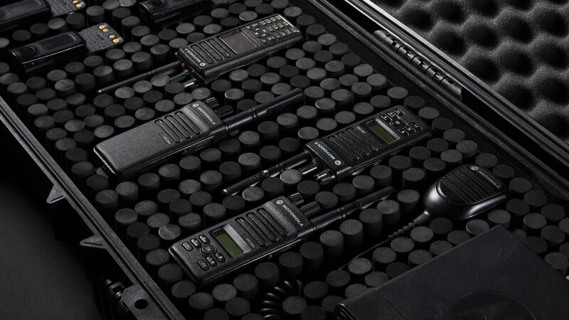 Multiple black two-way radios arranged in a padded equipment case with foam compartments.