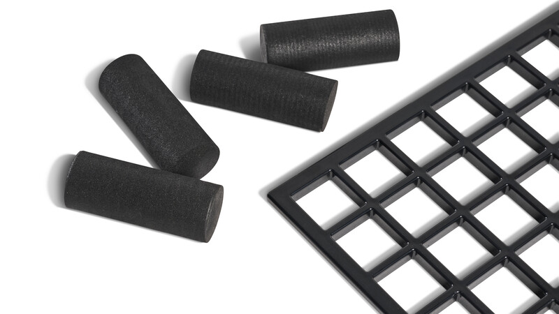 Four black cylindrical foam covers and a black grid pad arranged on white background.