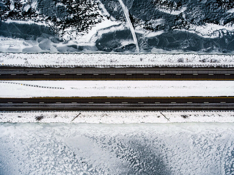 Aerial view of railroad tracks running through snow-covered landscape with forested areas.