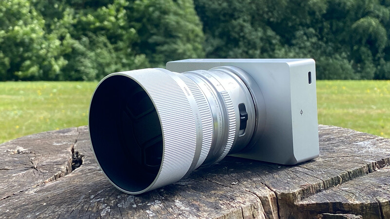 White smartphone with large telephoto lens attachment mounted on wooden log outdoors.