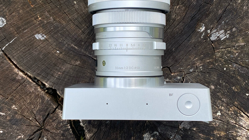 White mirrorless camera body with attached silver telephoto lens, viewed from above on a weathered wooden surface.