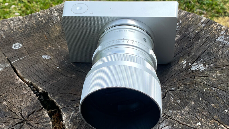 Silver telephoto lens attached to smartphone mounted on weathered tree stump outdoors.
