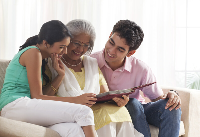 Three people viewing a tablet together on a sofa in bright natural light.