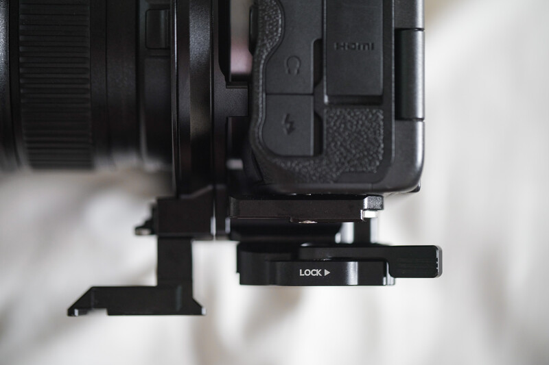 Close-up of camera body with L-bracket mounted underneath, showing lock lever and attachment hardware.