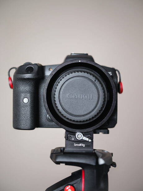 Canon mirrorless camera mounted on a tripod head against a neutral backdrop.