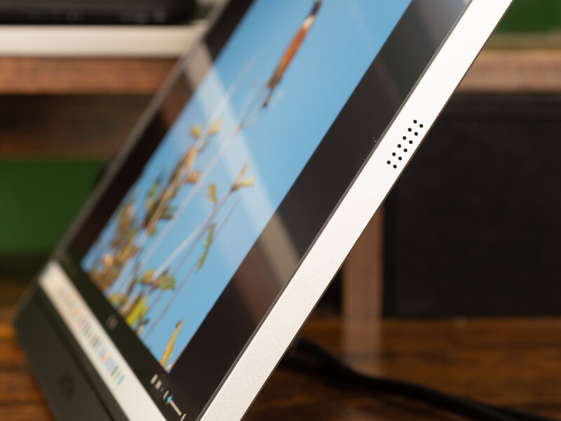 Close-up of tablet display showing landscape photograph with blue sky and golden field, angled on wooden surface.