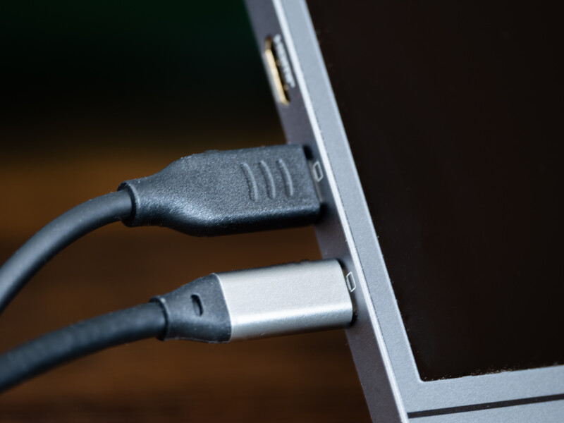 Two USB cables connected to the side of a laptop, showing a USB-A port and USB-C connector against a blurred background.