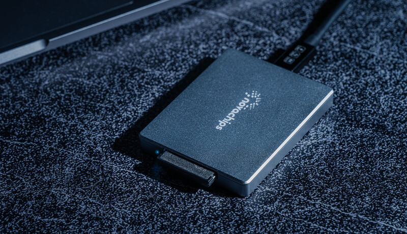 Dark external solid-state drive with cable on textured surface.