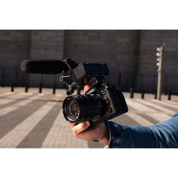 Filmmaker holding a mirrorless cinema camera with mounted microphone and monitor on an urban street.