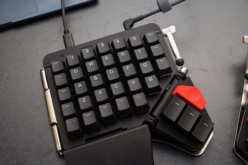Compact mechanical keyboard with detachable numpad featuring black keys and red accent key on dark desktop.
