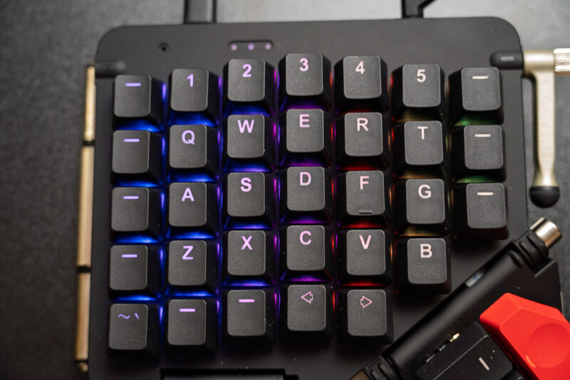 Mechanical gaming keyboard with illuminated keys in blue and purple lighting, showing QWERTY layout with numeric row and function keys.