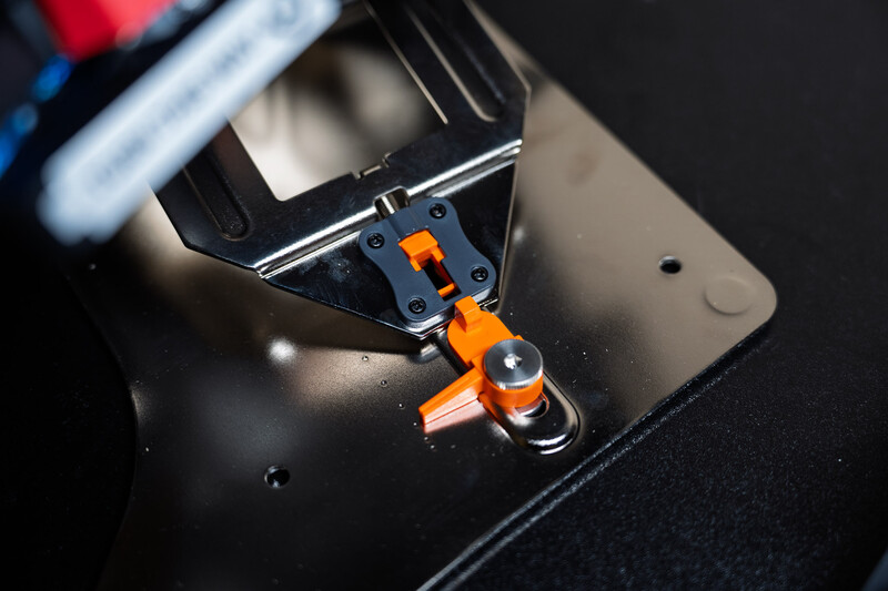 Close-up of a 3D printer nozzle with orange extruder assembly printing on a black build plate.