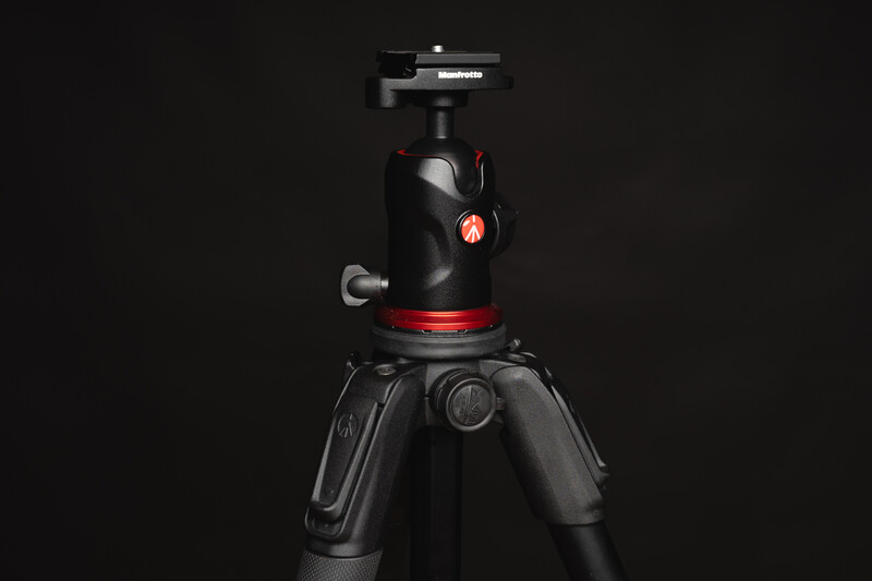 Professional tripod with ball head and red accents against a black background.