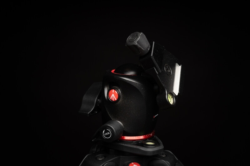 Professional tripod head with red accents against a black background, illuminated with studio lighting.