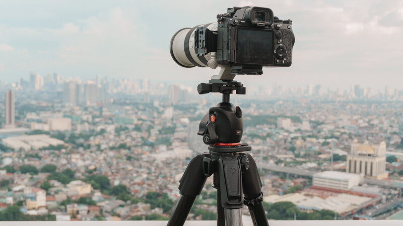 DSLR camera mounted on tripod overlooking expansive cityscape with river and urban sprawl.