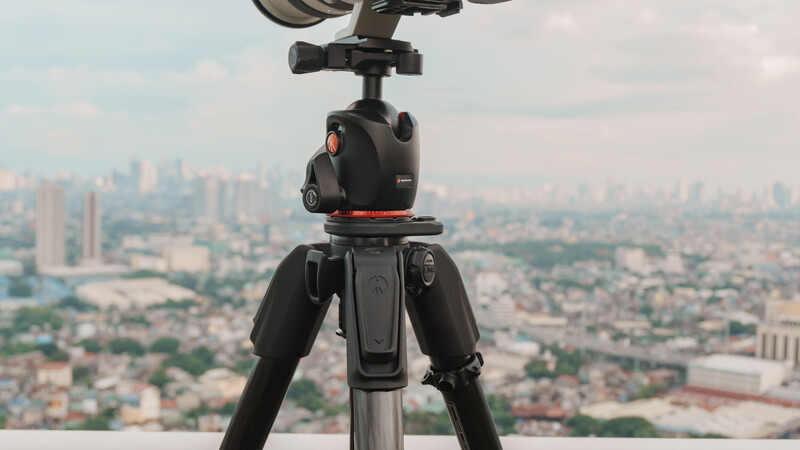 Professional ball head mounted on tripod legs overlooking a sprawling cityscape below.