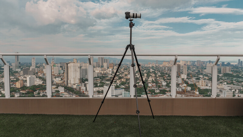 Camera on tripod positioned on rooftop overlooking urban cityscape with high-rise buildings.