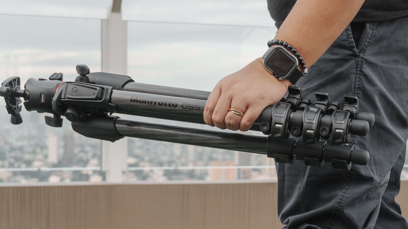 Person holding a tripod leg with fluid head against an urban skyline backdrop.