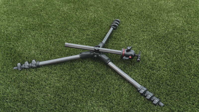 Professional camera tripod with adjustable legs spread in an X-formation on green grass.