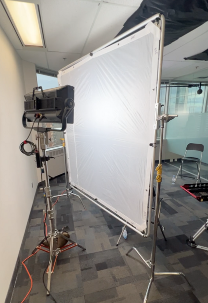 Professional film lighting setup with large diffusion panel and mounted studio light on tripod in studio space.