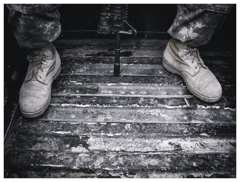 Person wearing suede boots standing on weathered wooden planks in black and white.