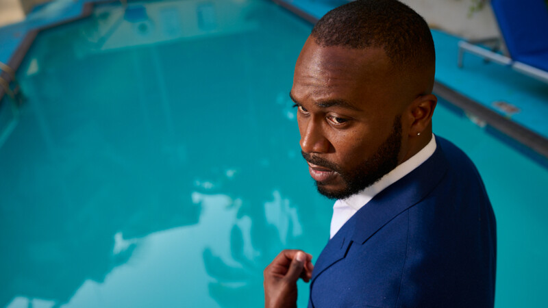 Professional man in navy blazer and white shirt posed against a bright turquoise blue wall.
