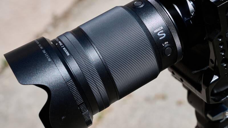 Telephoto lens with hood attached mounted on a mirrorless camera body against a blurred background.