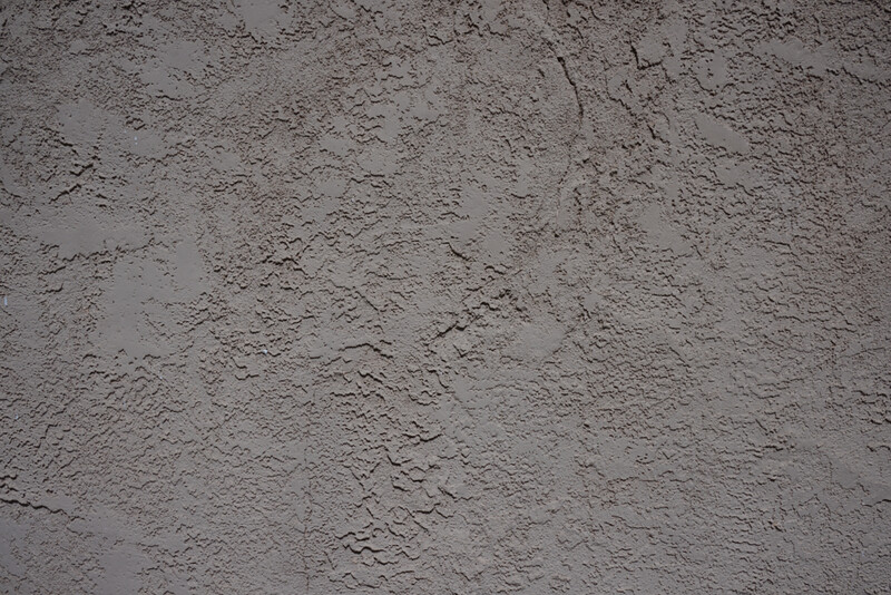 Close-up of rough, textured concrete or cement surface with irregular cracks and variations in tone.